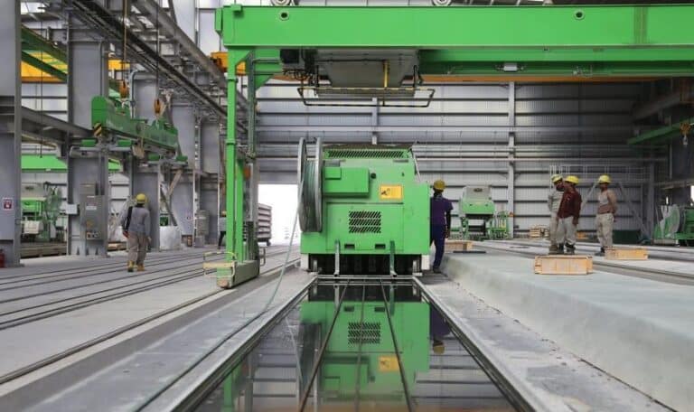 Green industrial machinery and equipment in a large factory space, with workers in the background