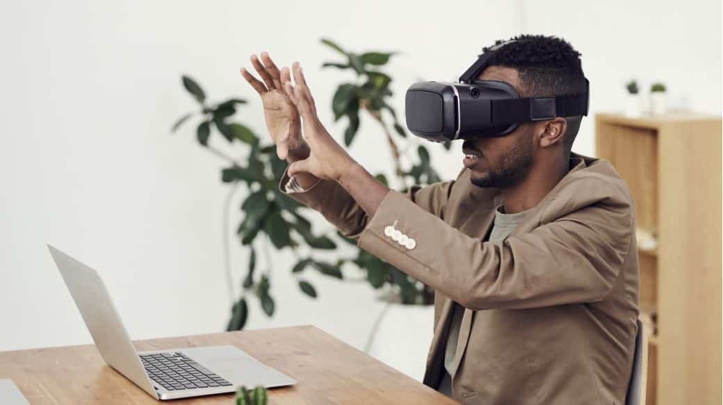 Man using virtual reality headset while working at a desk with a laptop