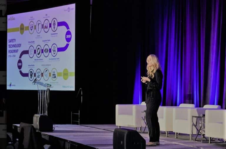 Image of a woman presenting on stage, with a large projection screen displaying a 'Safety Technology Roadmap' behind her
