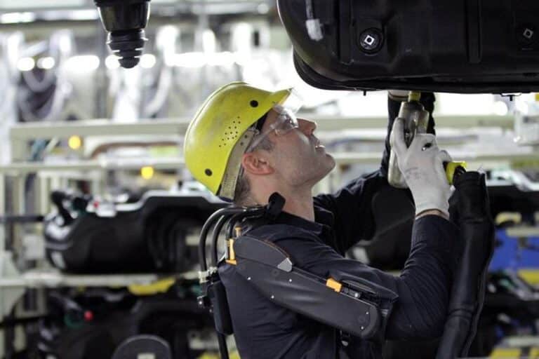 A factory worker in a yellow hardhat and safety gear working on a piece of heavy machinery