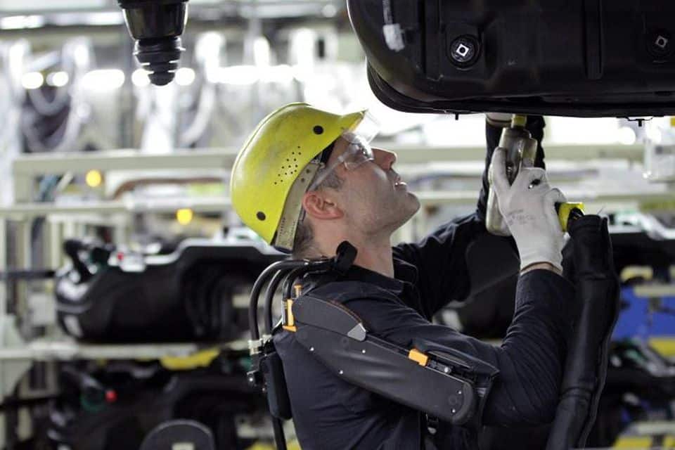 A factory worker in a yellow hardhat and safety gear working on a piece of heavy machinery