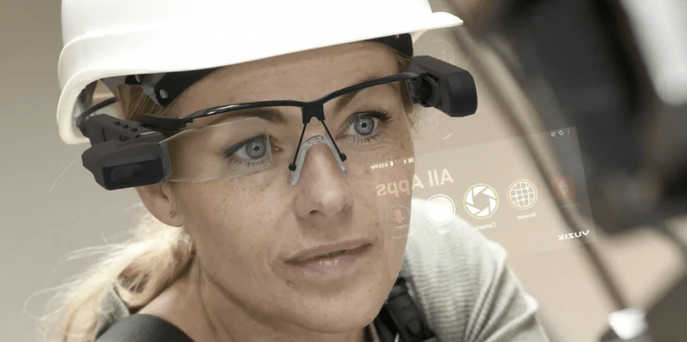 A woman wearing a hard hat and safety glasses with a facial display screen, representing technology and engineering fields