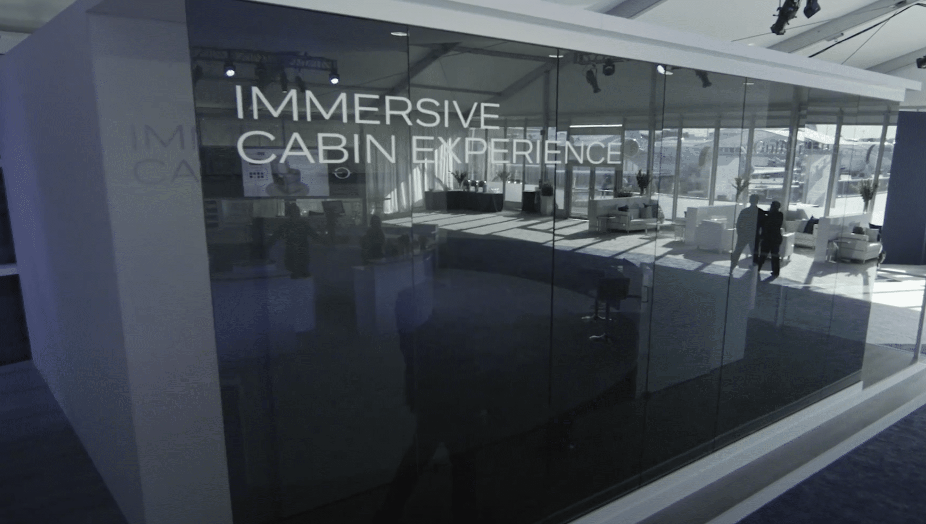 An interior view of an immersive cabin experience, with glass walls, modern furniture, and people visible inside