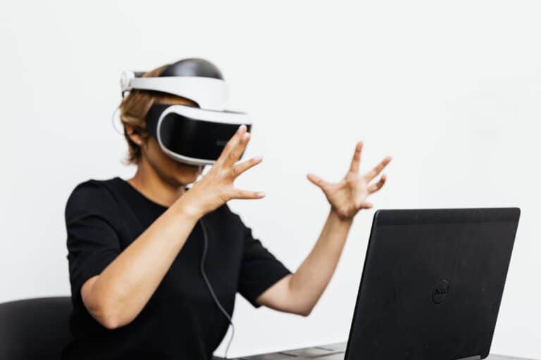 Person wearing virtual reality headset, gesturing with hands in front of laptop computer