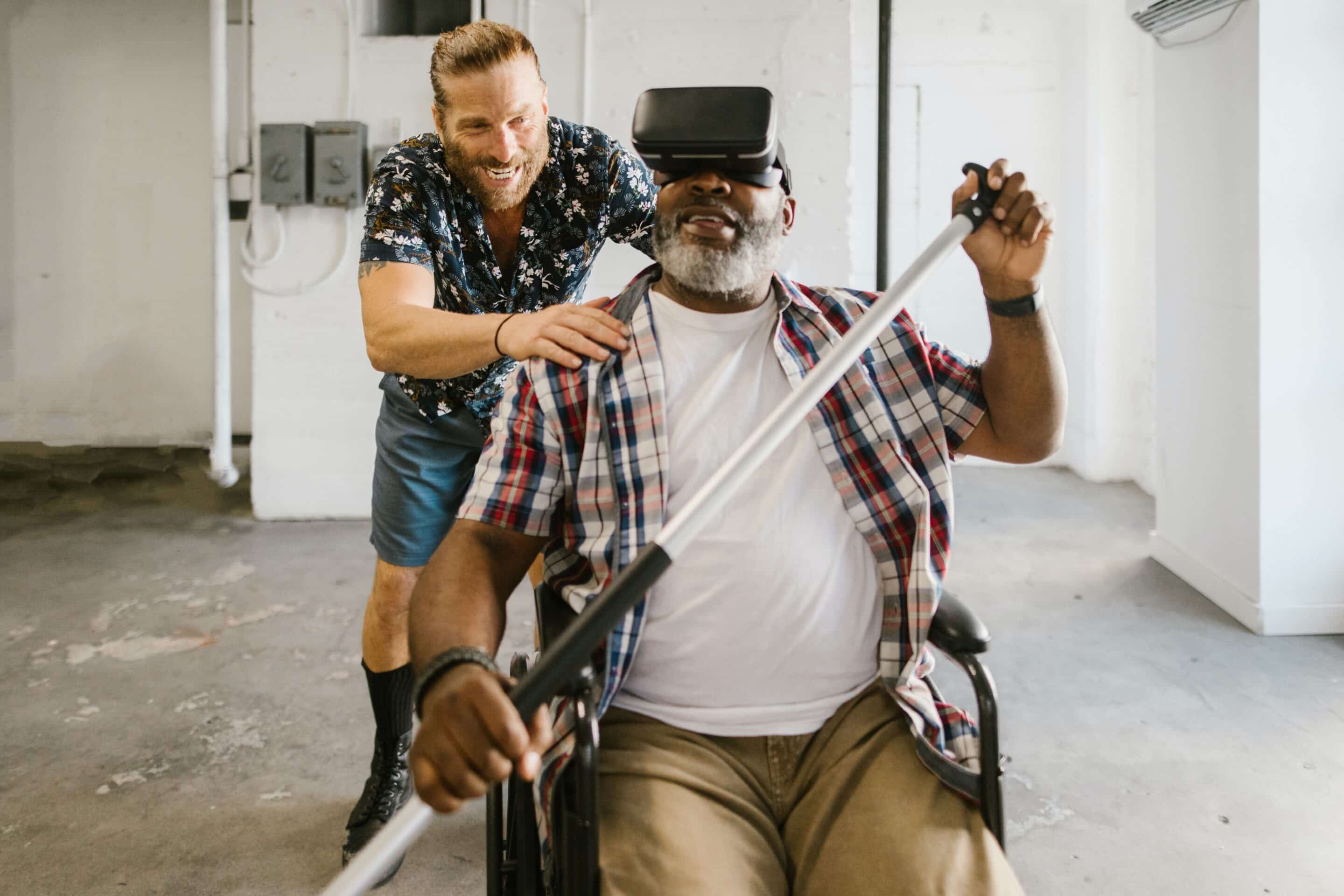 Two men, one in a floral shirt and the other in a wheelchair, interacting and smiling in a room