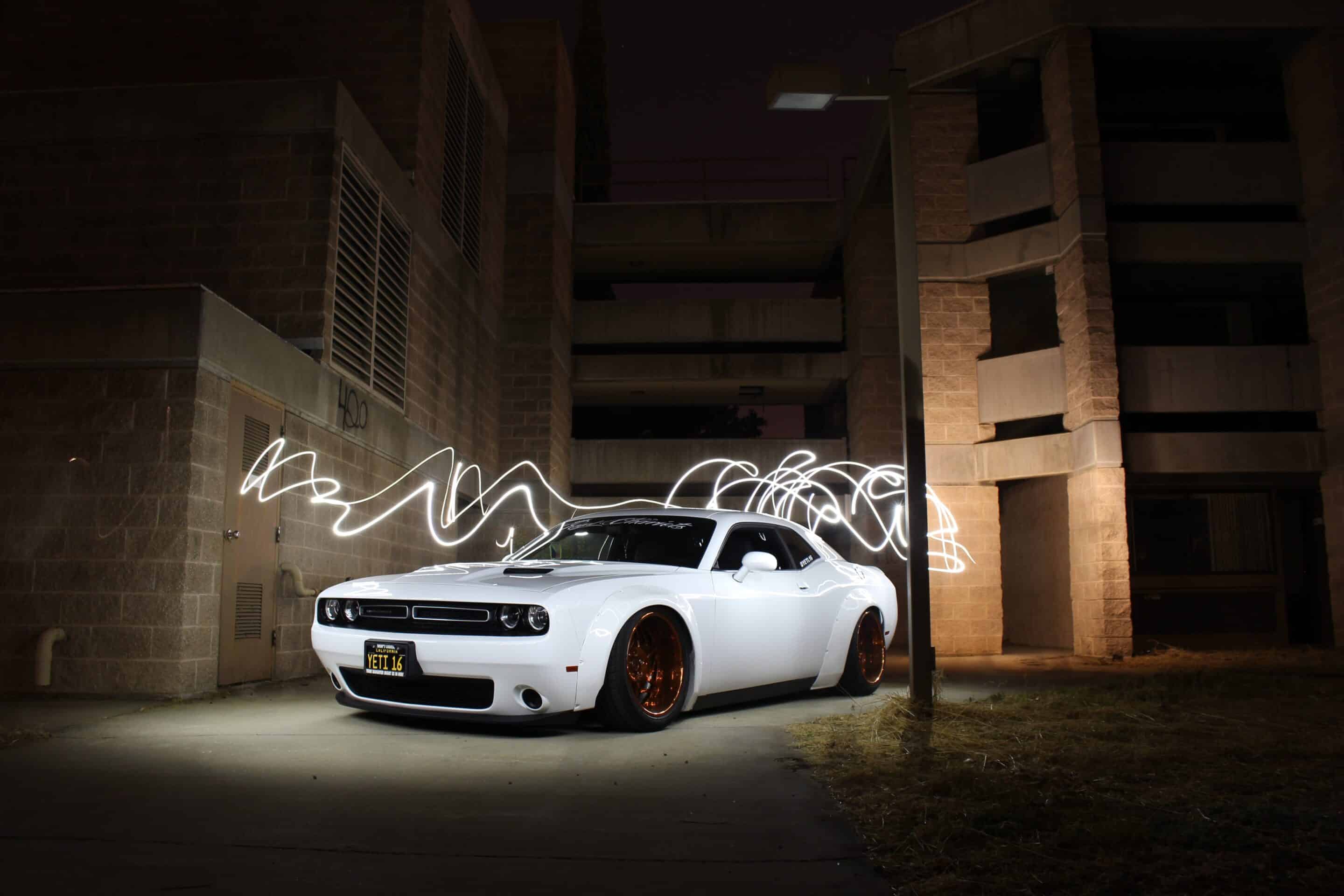 A white Dodge Challenger sports car with custom wheels parked in a dark alley with graffiti on the wall