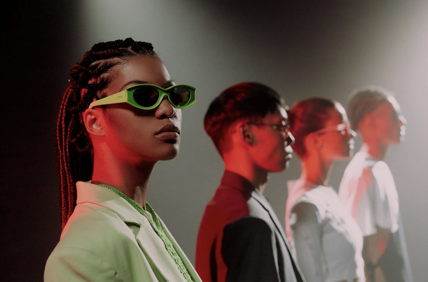 A group of young people posing on a dark stage, wearing stylish outfits and accessories.