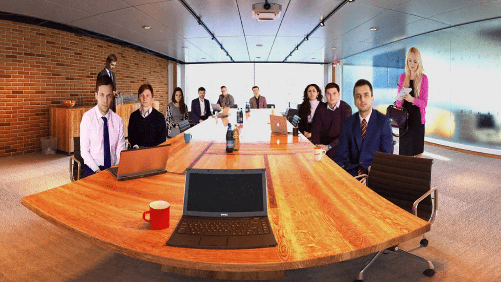 A group of business professionals in a conference room with a large wooden table, laptop, and various office supplies