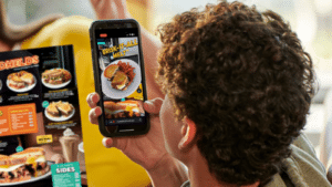 A person holding a mobile phone displaying an augmented reality image of a fast food brisk-it-all melt sandwich