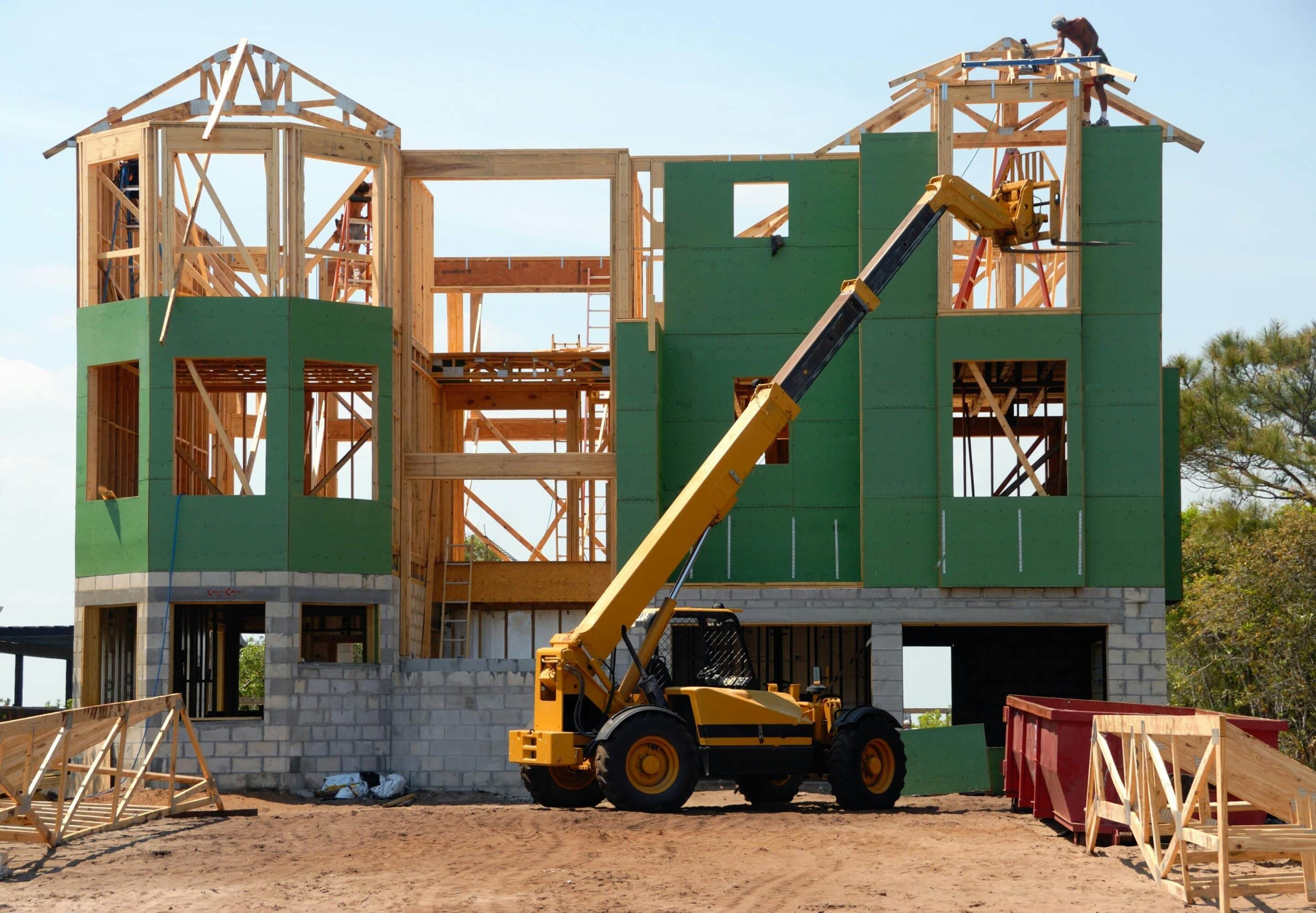 Construction site with wooden frame and yellow forklift, showcasing home building process